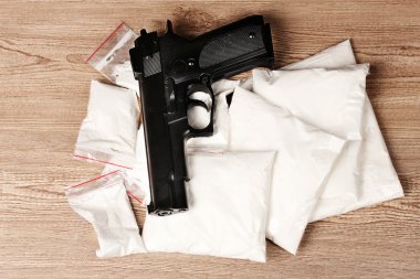 Cocaine in packages and handgun on wooden background clipart