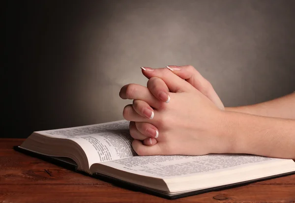 Hands folded in prayer over open russian Holy Bible on black background — Stock Photo, Image