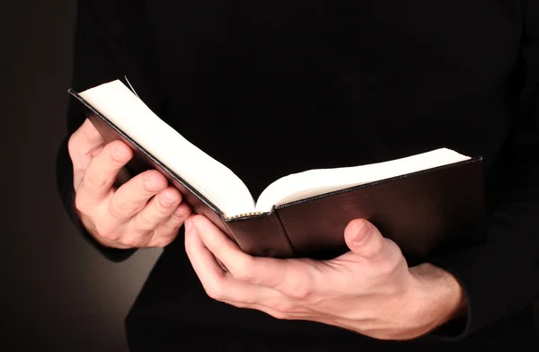 Mãos segurando bíblia russa aberta no fundo preto — Fotografia de Stock