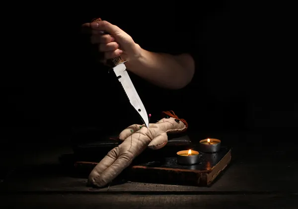 Кукла вуду, пронзённая ножом на деревянном столе при свете свечей — стоковое фото