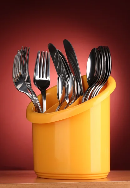 Кухонные столовые приборы, ножи, вилки и ложки желтого цвета стоят на красном фоне — стоковое фото
