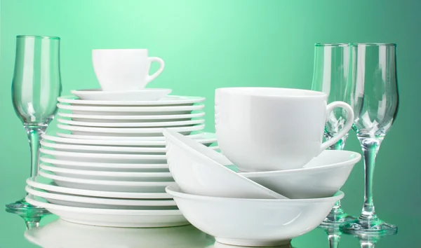 Clean plates, cups and glasses on green background — Stock Photo, Image