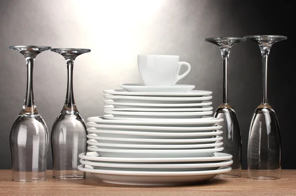 Saubere Teller, Gläser und Tassen auf Holztisch auf grauem Hintergrund — Stockfoto