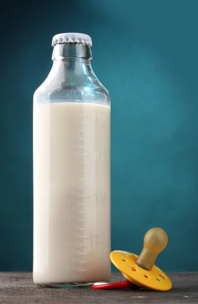 Bottiglia di latte e succhietto su tavolo di legno su fondo blu — Foto Stock
