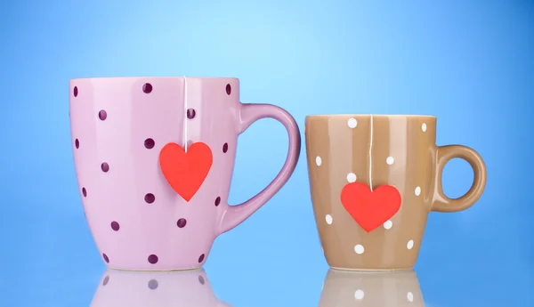 Två koppar och tepåsar med röda hjärtformade etikett på blå bakgrund — Stockfoto