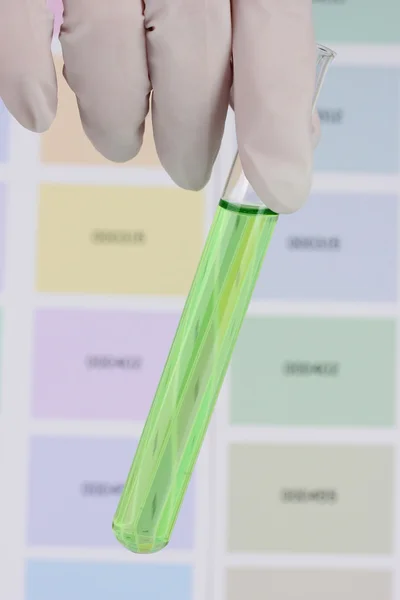 Tube with green liquid in hand on color samples background — Stock Photo, Image