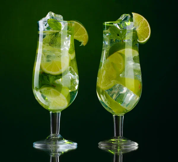 Vasos de cócteles con lima y menta sobre fondo verde — Foto de Stock