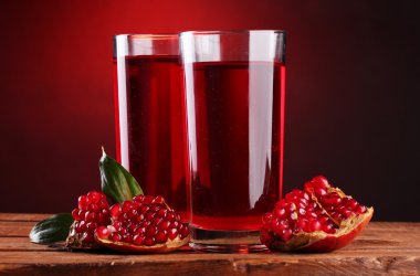 Ripe pomergranate and glasses of juice on wooden table on red background clipart