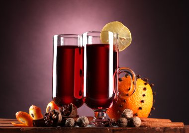 Mulled wine in the glasses, spice and orange on wooden table on purple back clipart