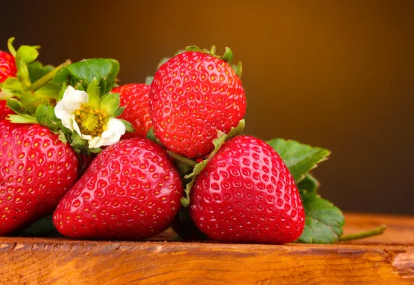 Erdbeeren mit Blättern auf Holztisch auf braunem Hintergrund — Stockfoto