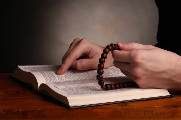 Hands holding wooden rosary over open russian holy bible on grey background — Stock Photo, Image