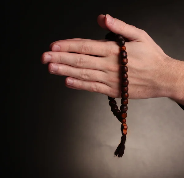 Manos sosteniendo rosario de madera sobre fondo gris — Foto de Stock