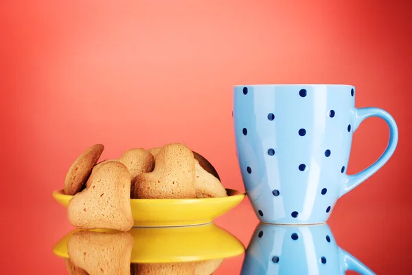 Herzförmige Kekse auf gelbem Teller und Tasse auf rotem Hintergrund — Stockfoto