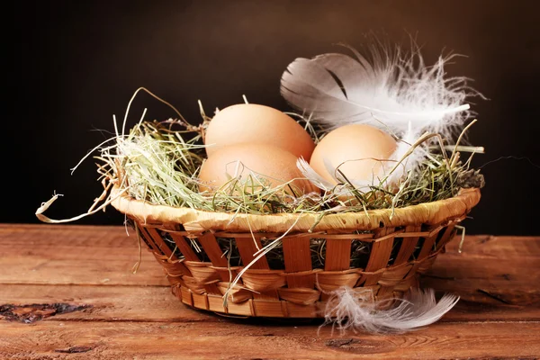 Chicken eggs in a nest on wooden table on brown background — Stock Photo, Image