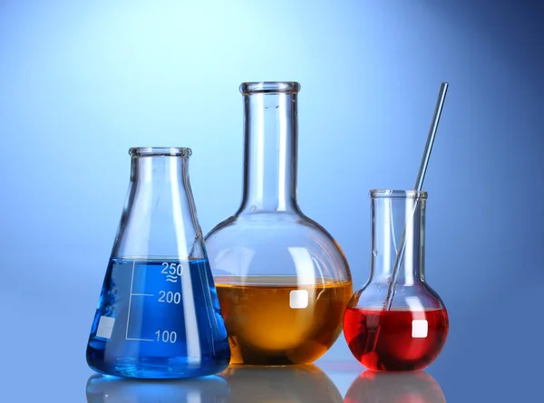 Três frascos com líquido colorido com reflexão sobre fundo azul — Fotografia de Stock