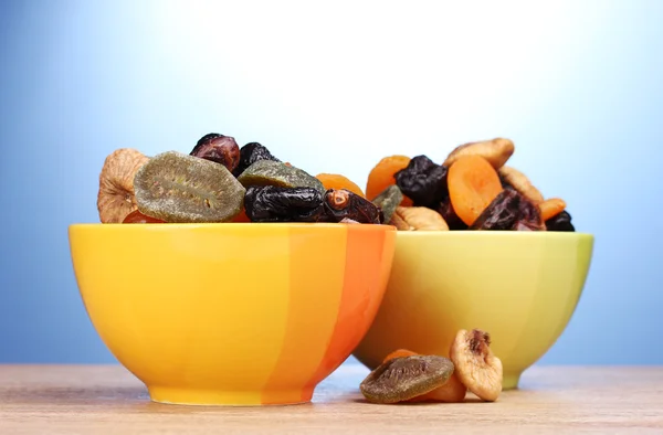 Frutas secas en cuencos brillantes sobre mesa de madera sobre fondo azul —  Fotos de Stock