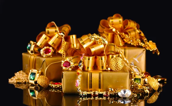 Verschiedene Goldschmuck und Geschenke auf schwarzem Hintergrund — Stockfoto