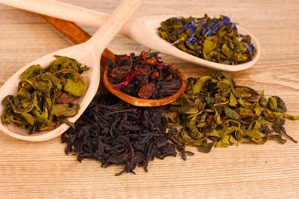 Verschiedene Arten von trockenem grünem und schwarzem Tee in Löffeln auf Holzgrund — Stockfoto