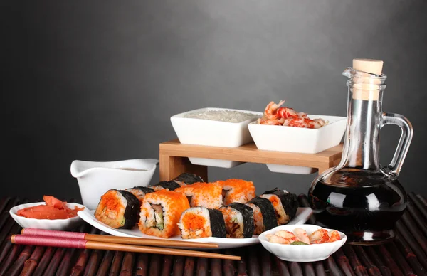 Heerlijke sushi op plaat, eetstokjes, sojasaus, vis en garnalen op bamboe — Stockfoto