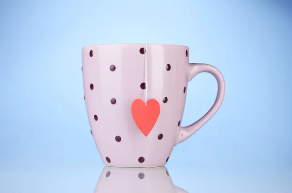 Розовая чашка и пакетик чая с красной сердечной маркировкой на синем фоне — стоковое фото
