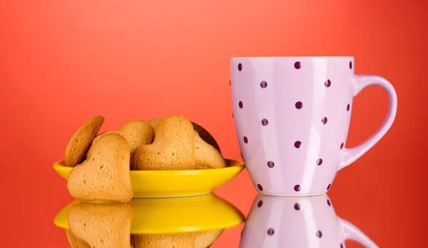 Heart-shaped cookies on yellow plate and cup on red background — Stock Photo, Image