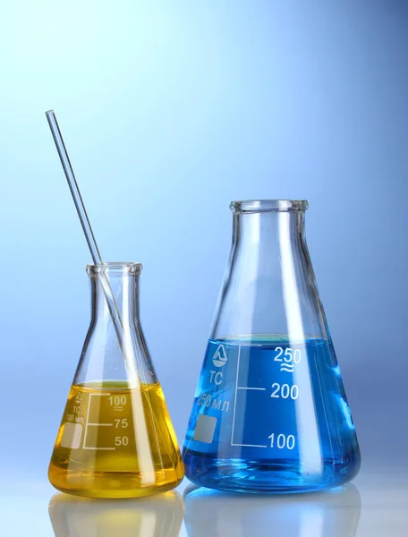 Dos frascos con líquido amarillo y azul con reflexión sobre fondo azul — Foto de Stock