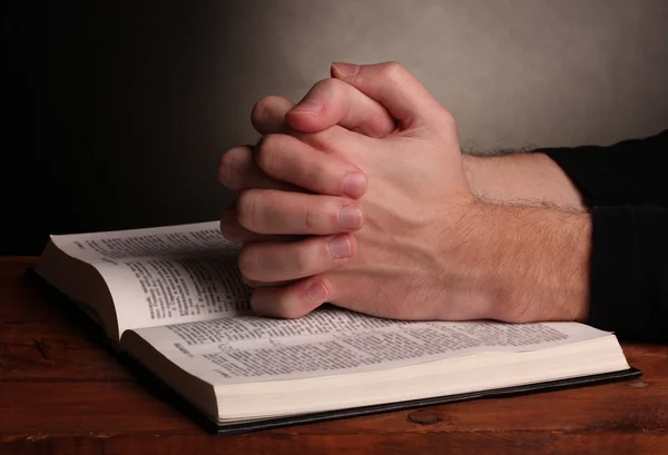 Τα χέρια διπλωμένα στην προσευχή πάνω από μια Αγία Γραφή στο ξύλινο τραπέζι σε γκρι φόντο — Φωτογραφία Αρχείου