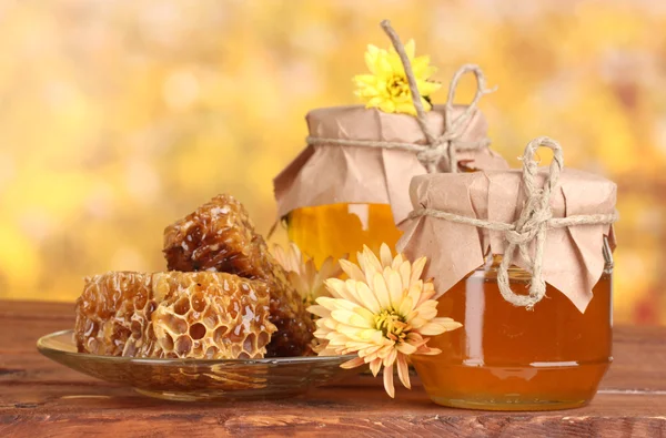 Két üveget, méz, lépek, és fából készült drizzler az asztalon, a sárga backgro — Stock Fotó