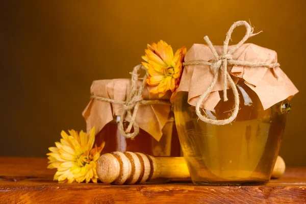 Dos frascos de miel y rociador de madera sobre la mesa sobre fondo amarillo —  Fotos de Stock