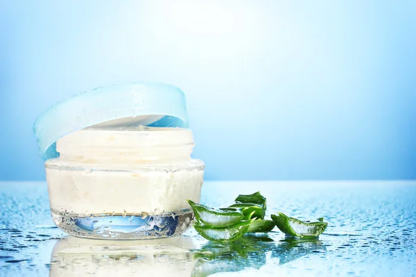 Vaso di vetro aperto di crema e aloe su sfondo blu con goccioline d'acqua — Foto Stock