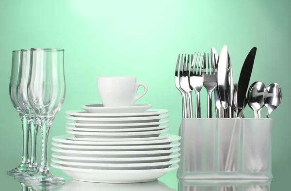Clean plates, glasses, cup and cutlery on green background — Stock Photo, Image