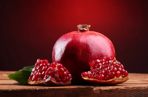 Mogen granatäpple frukt med lämnar på träbord på röd bakgrund — Stockfoto