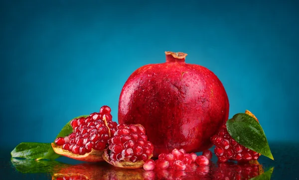 Ripe pomegranate fruit with leaves on blue background — Stock Photo, Image