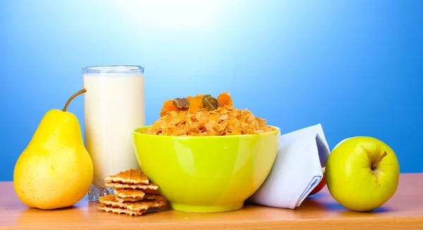 Tasty cornflakes in green bowl and glass of milk on wooden table on blue ba — Stock Photo, Image