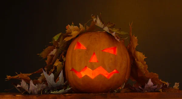 Calabaza de Halloween y hojas de otoño sobre mesa de madera sobre fondo marrón — Foto de Stock