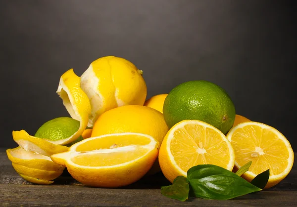 Ripe lemons and limes with leaves on wooden table on grey background — Stock Photo, Image
