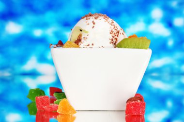 Delicious vanilla ice cream with chocolate and fruits in bowl on blue backg clipart