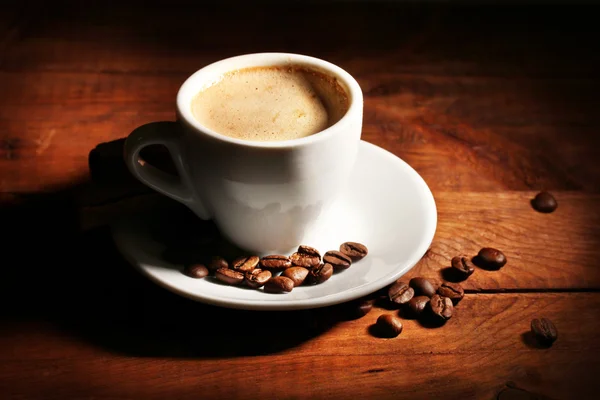 Чашка з кавою та кавовими зернами на дерев'яному столі — стокове фото