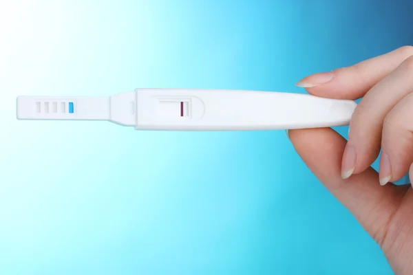 Prueba de embarazo en la mano sobre fondo azul — Foto de Stock