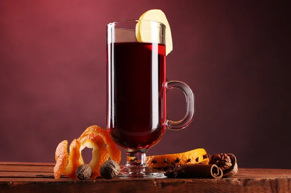 Vin brulè nel bicchiere, spezie e limone su fondo rosso — Foto Stock