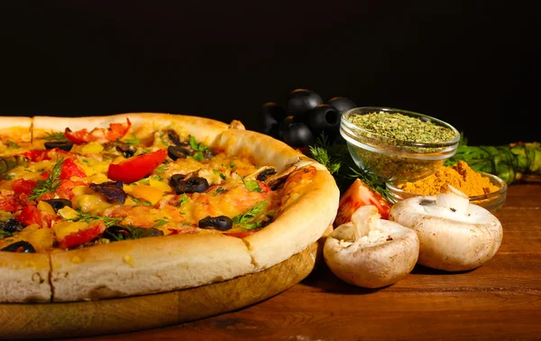 Herkullinen pizza, vihannekset ja mausteet puupöydällä ruskealla taustalla — kuvapankkivalokuva