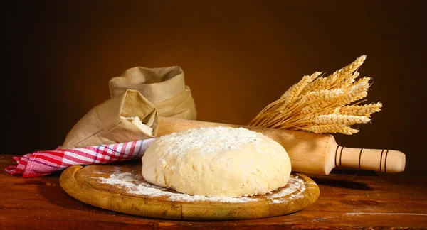 Pâte et sacs avec farine sur table en bois sur fond marron — Photo