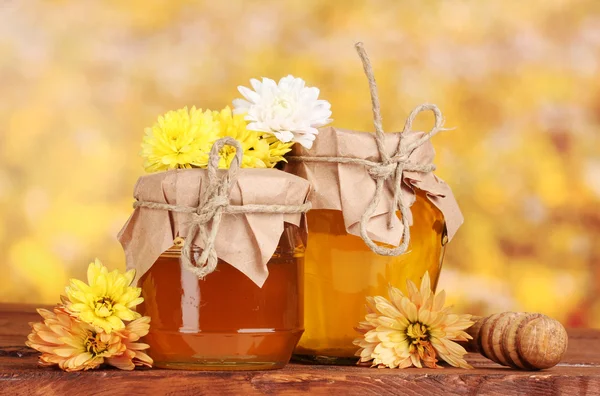 Two jars of honey and wooden drizzler on table on yellow background — Stock Photo, Image