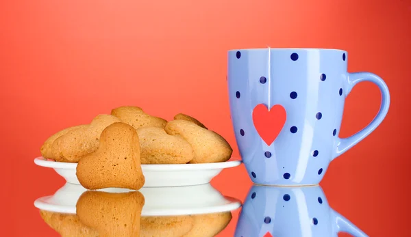 Ciasteczka w kształcie serca na płytkę i Puchar z torebkę na czerwonym tle — Zdjęcie stockowe