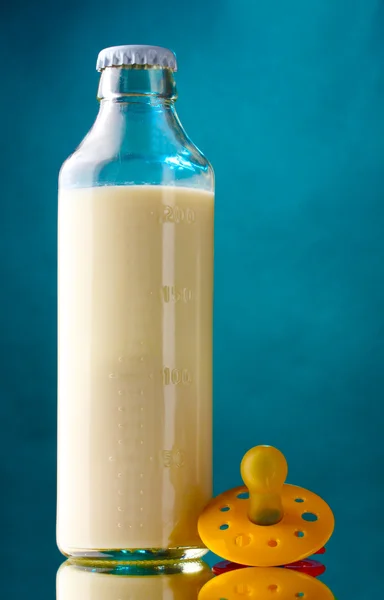 Láhev mléka a dudlík na modrém pozadí — Stock fotografie