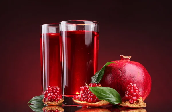 Ripe pomergranate and glasses of juice on red background — Stock Photo, Image