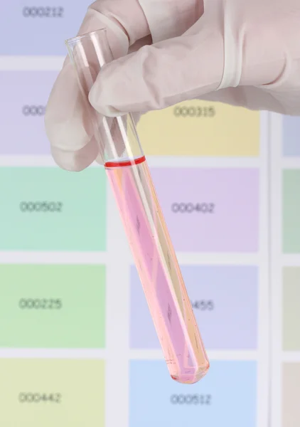 Rör med rosa vätska i handen på färg prover bakgrund — Stockfoto