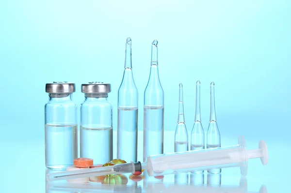 Stříkačka s lékařskou ampulí a tablety na modrém pozadí — Stock fotografie