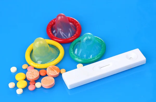 Födelse kondomer, graviditetstest och piller på blå bakgrund — Stockfoto