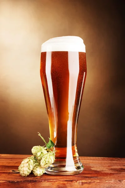 Piwo w szkło i zielony hop na drewnianym stole na brązowym tle — Zdjęcie stockowe